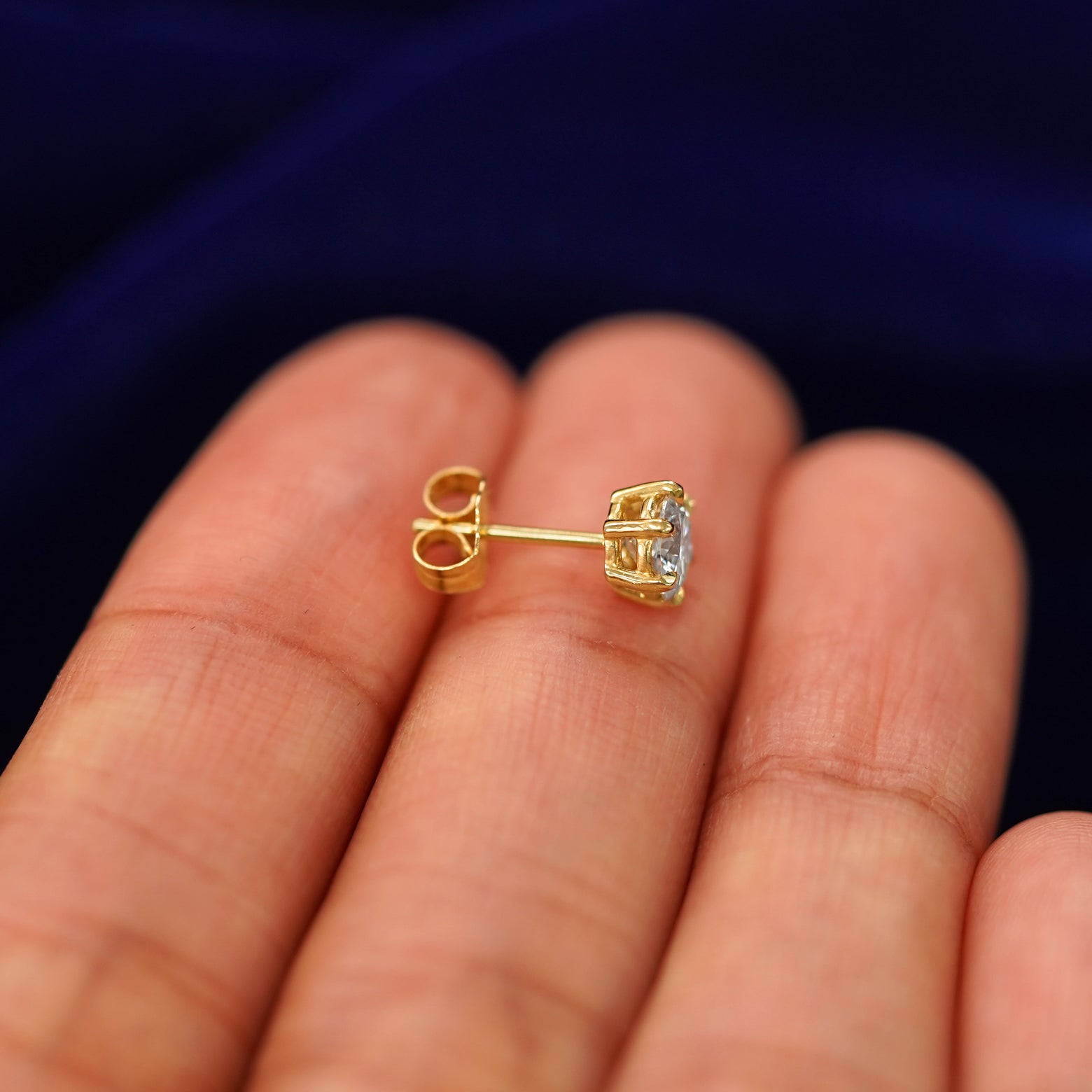 A 14k gold clear 5mm Moissanite Earring sitting sideways on a model's fingertips to show detail
