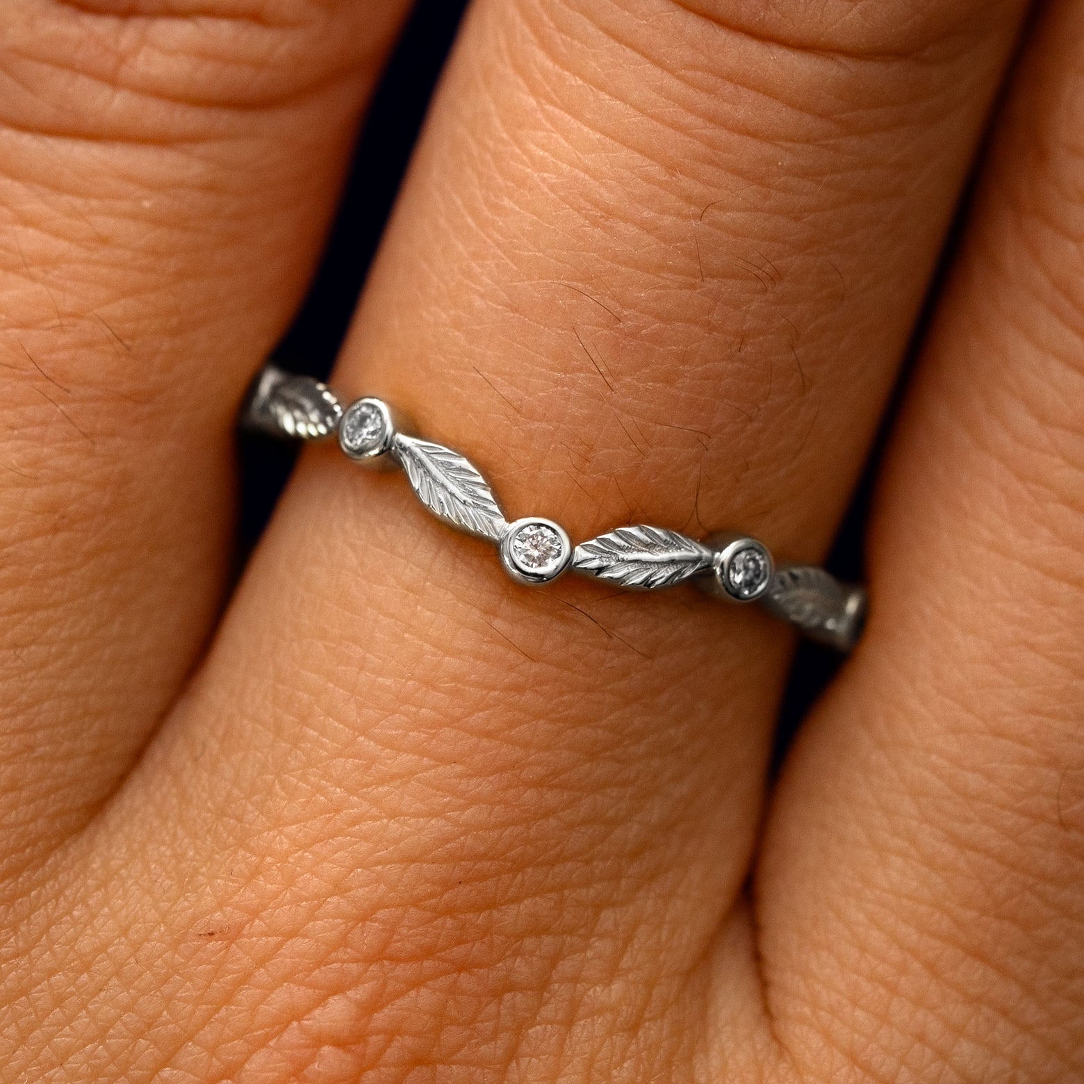 Close up view of a model's fingers wearing a 950 platinum Chevron Leaves and Round Diamonds Band