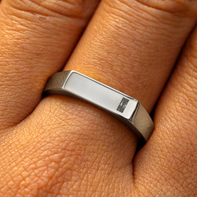 A model's finger wearing a platinum baguette salt and pepper diamond rectangular signet ring