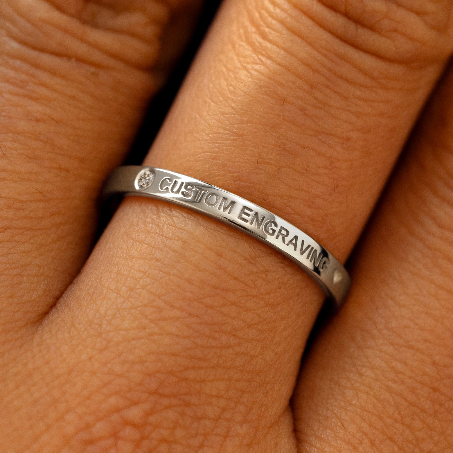 A model's finger wearing a diamond 950 platinum flush gemstone industrial band the words custom engraving on the top