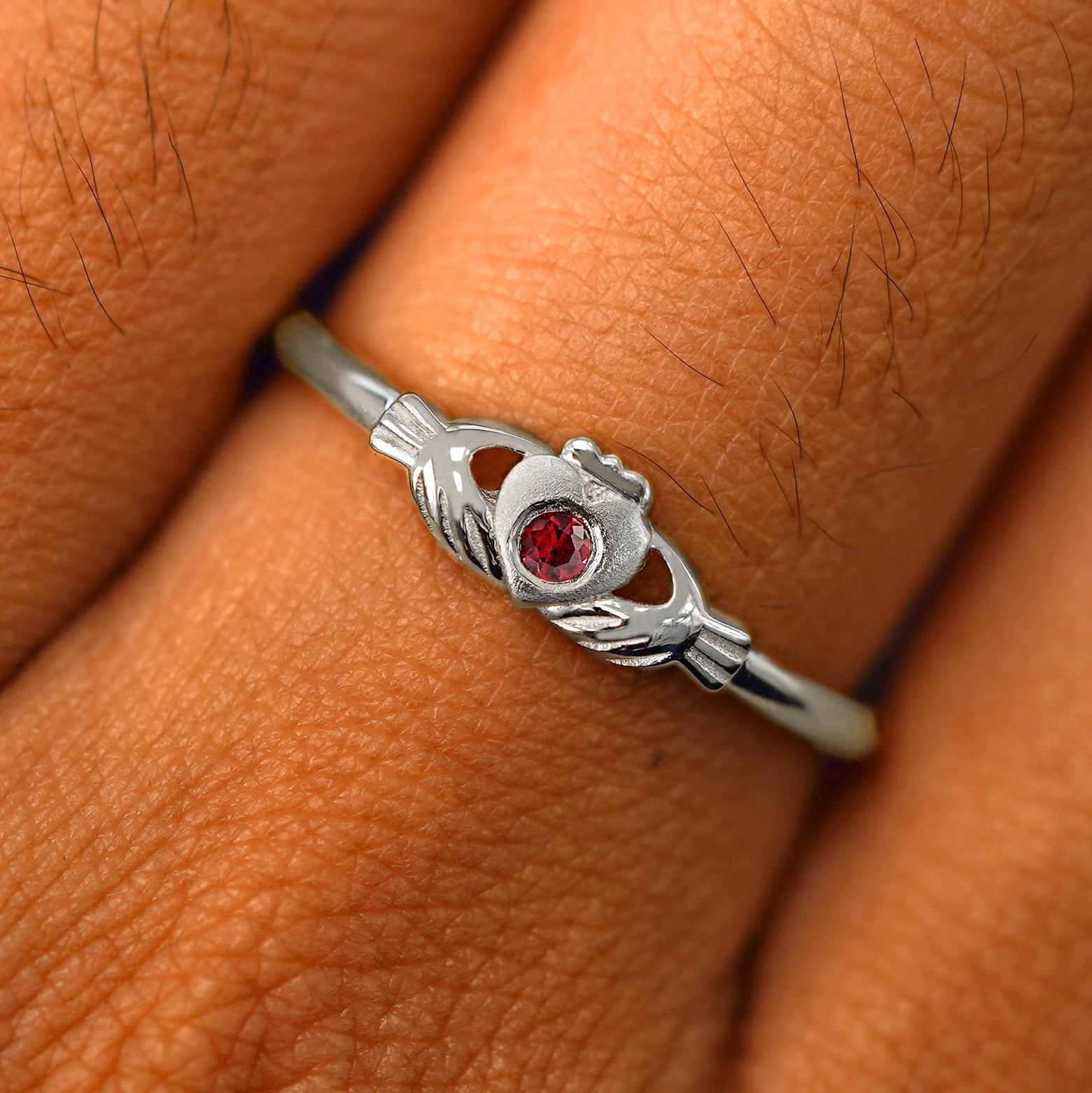 Close up view of a model's fingers wearing a 950 platinum garnet Thin Gemstone Claddagh Ring