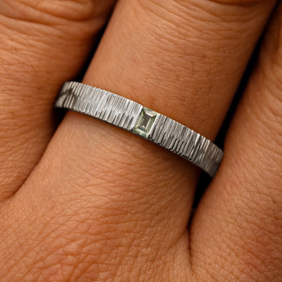 Close up view of a model's fingers wearing a 950 platinum Baguette Green Sapphire Wood Band