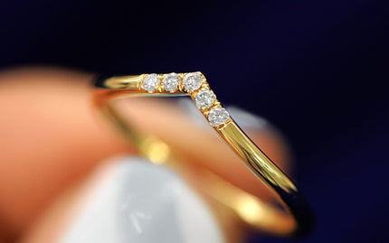 Cloe up view of a yellow gold chevron diamond band held between a models fingers