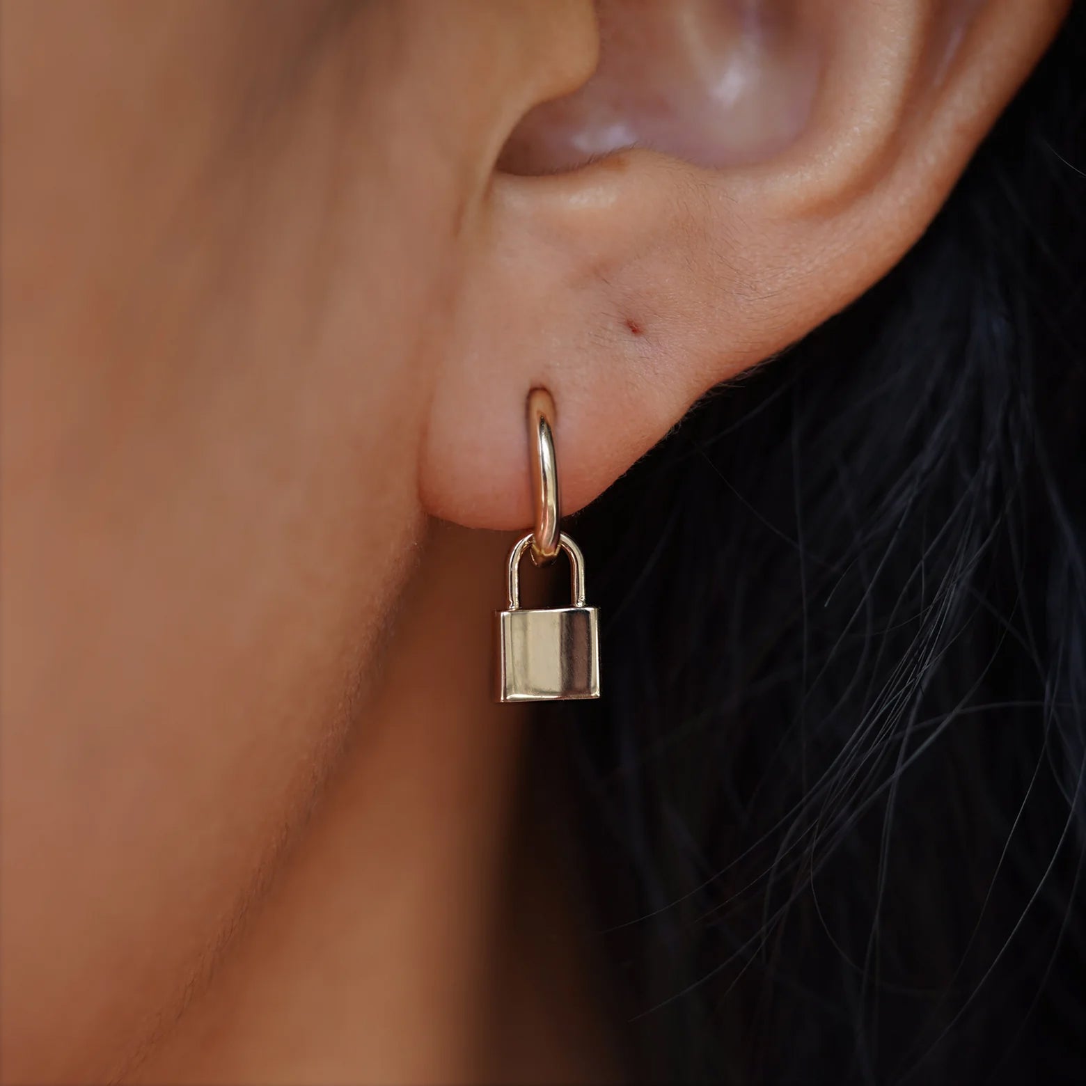A 14 karat solid champagne gold Lock Charm resting on the back of a model's hand