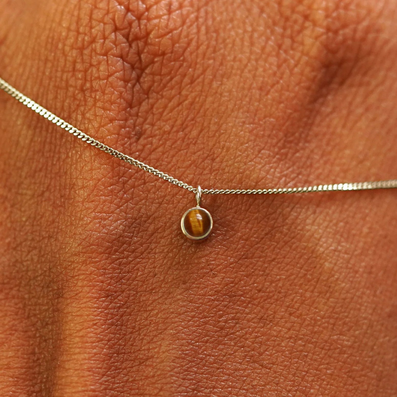 Close up view of a 14k champagne gold Tiger Eye Necklace draped across the back of a model's hand
