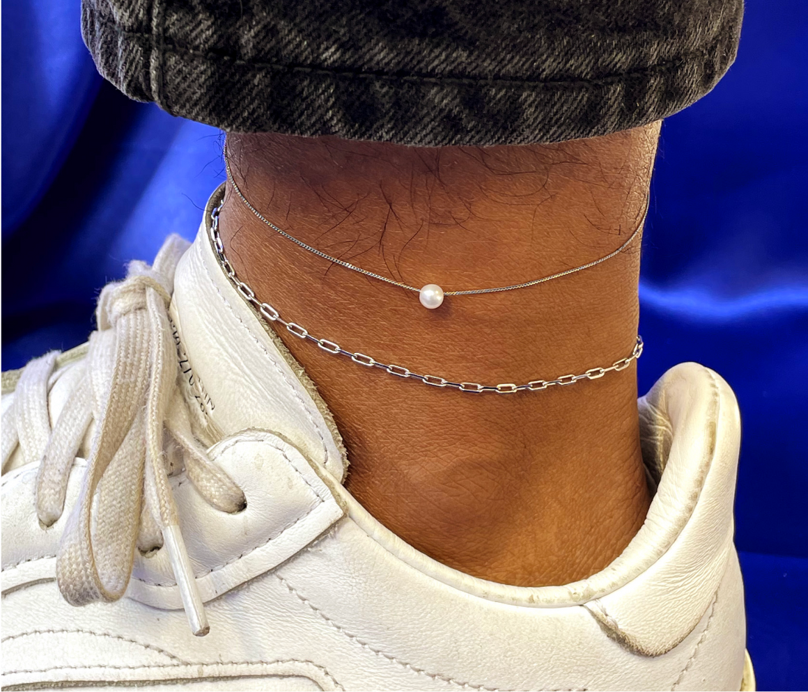 Close up view of a model's ankle wearing a white gold Butch Anklet and a Small Pearl Slide Bracelet as an anklet