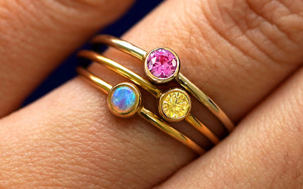 Close up view of a models hand wearing a stack of solitaire gemstone rings