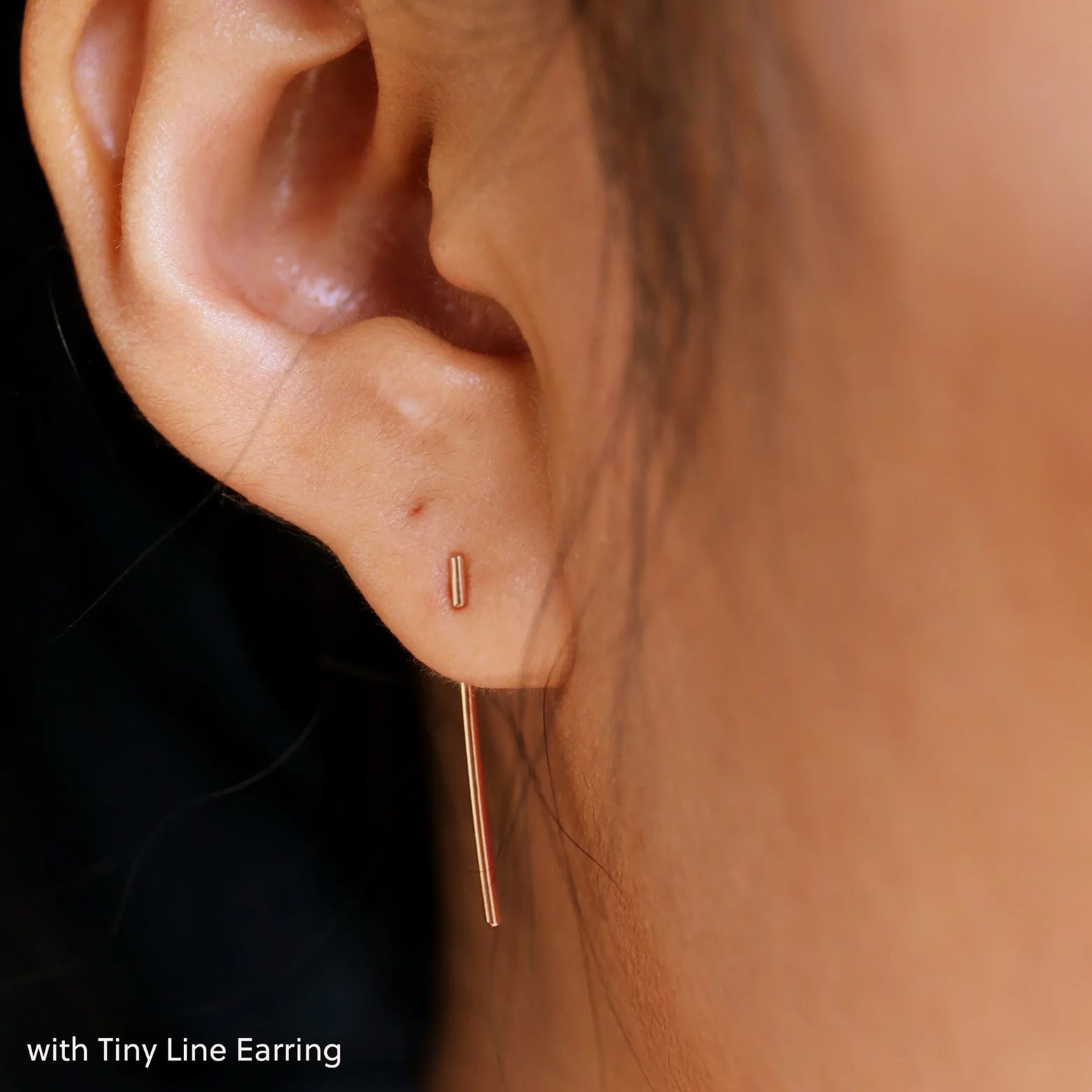Close up view of a model's ear wearing a rose gold Line Jacket with a Tiny Line Earring