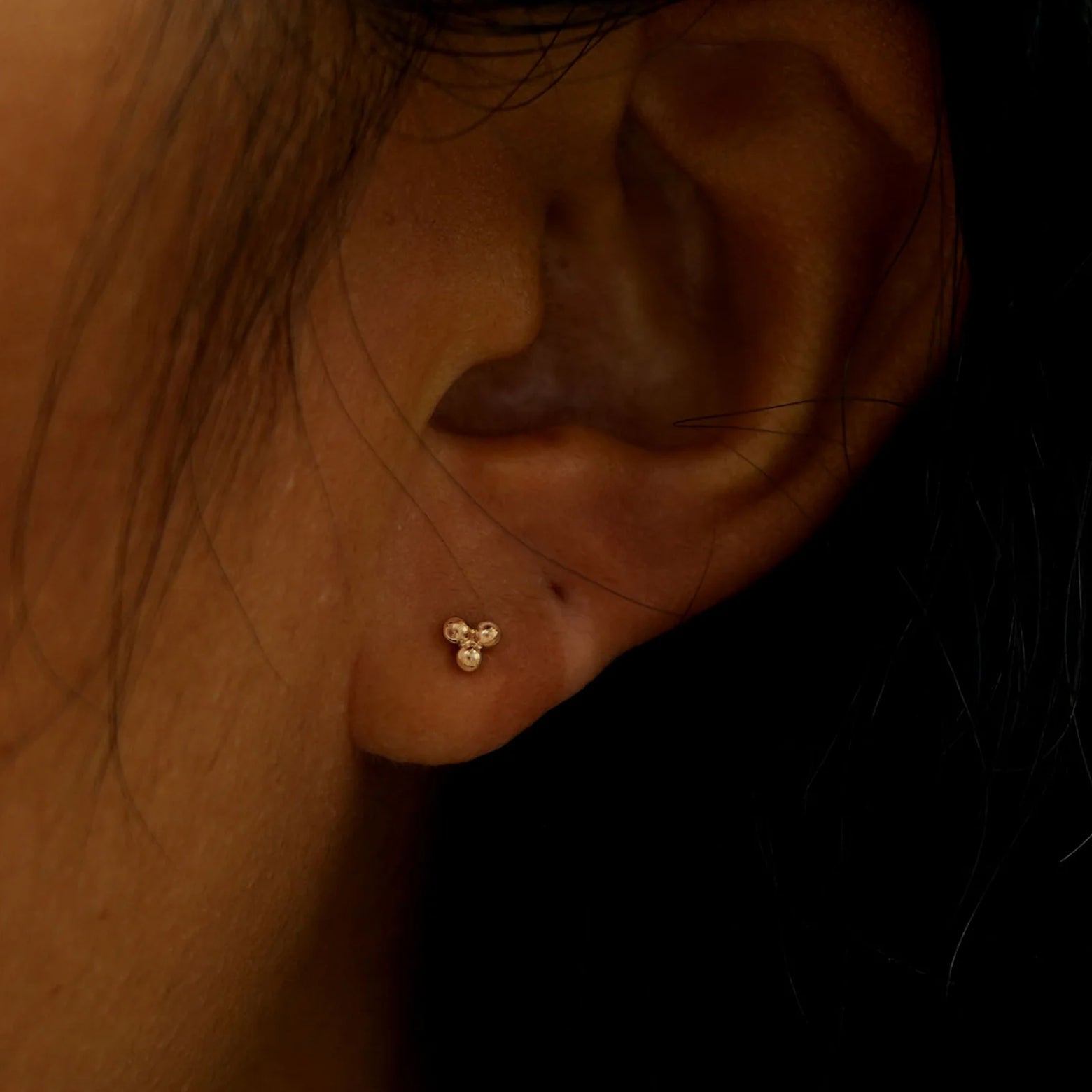Close up view of a model's ear wearing a rose gold Ball Trio Earring