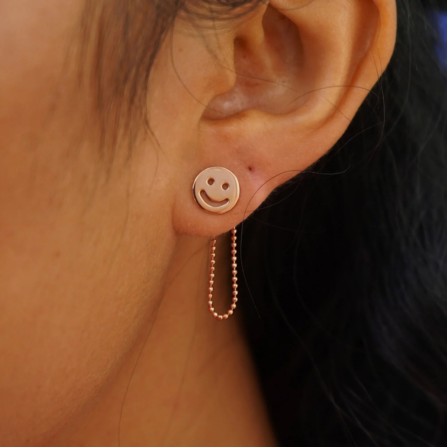 Close up view of a model's ear wearing a rose gold Connector with both attached behind a Smiley Face Earrings