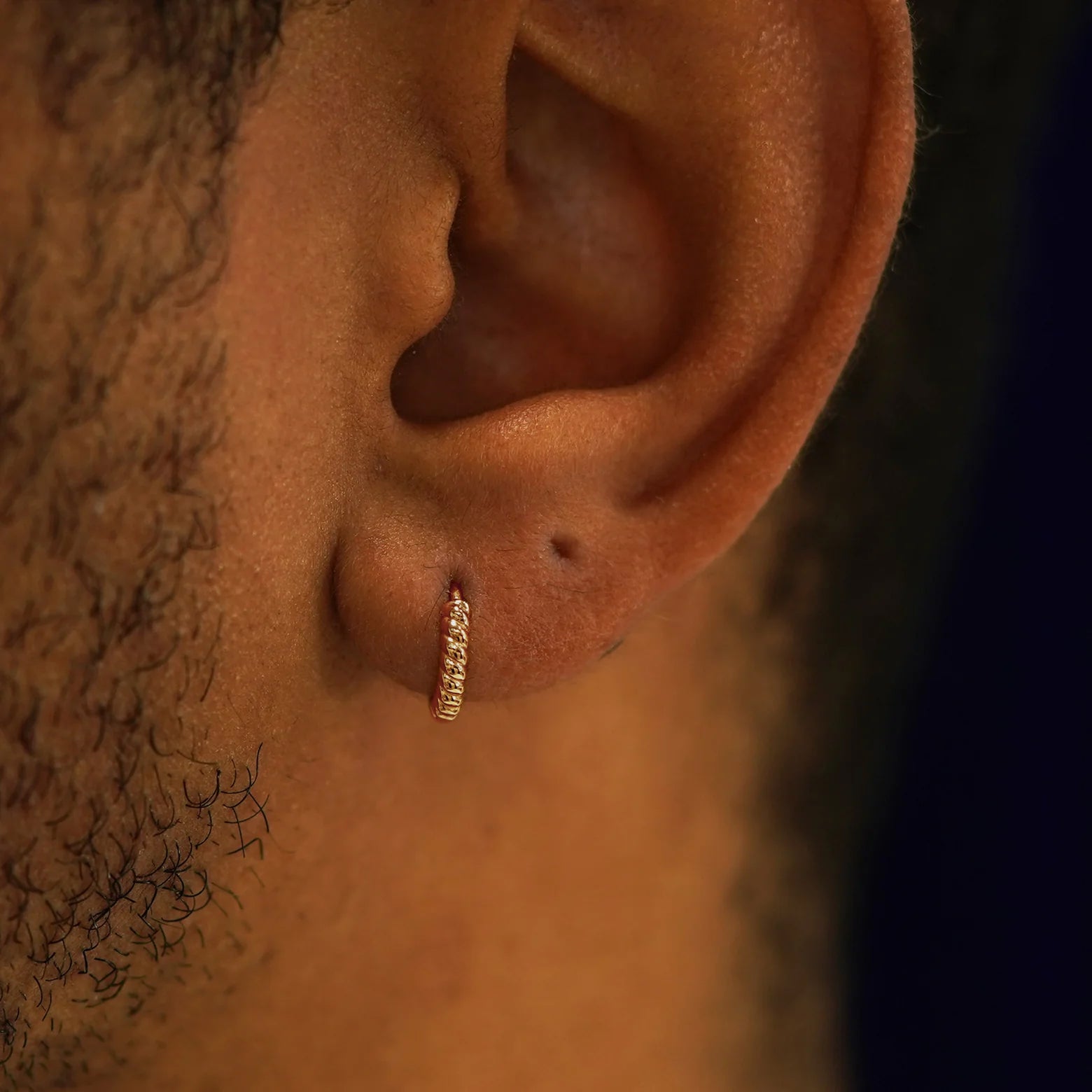 A model's ear wearing a 14k rose gold Mini Rope Huggie Hoop Earring
