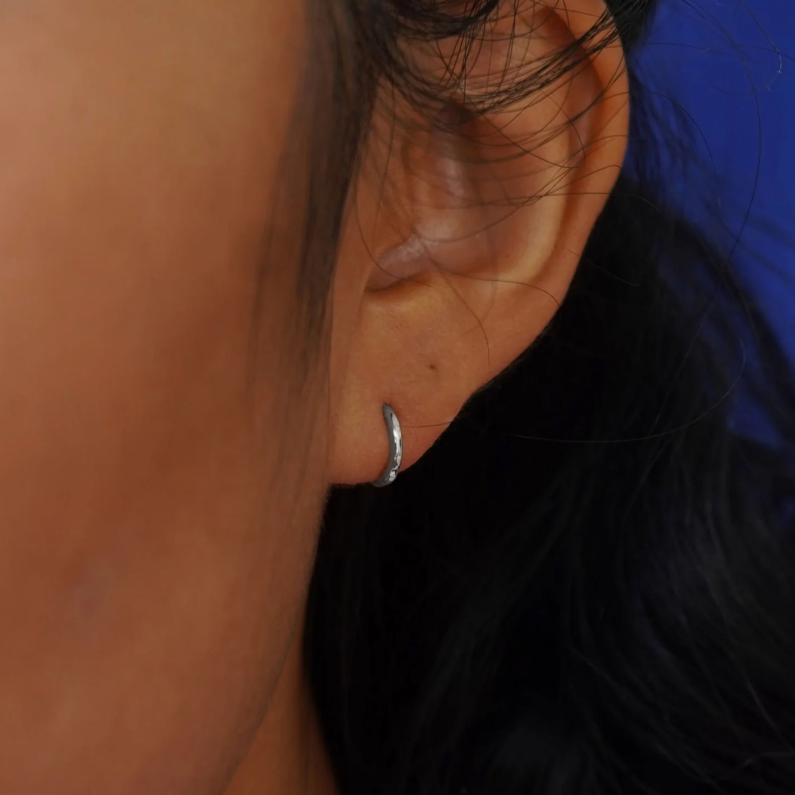 Close up view of a model's ear wearing a white gold Mini Curvy Huggie Hoop