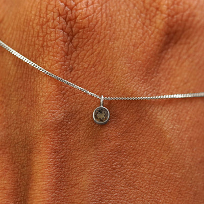 Close up view of a 14k white gold Smoky Quartz Necklace draped across the back of a model's hand