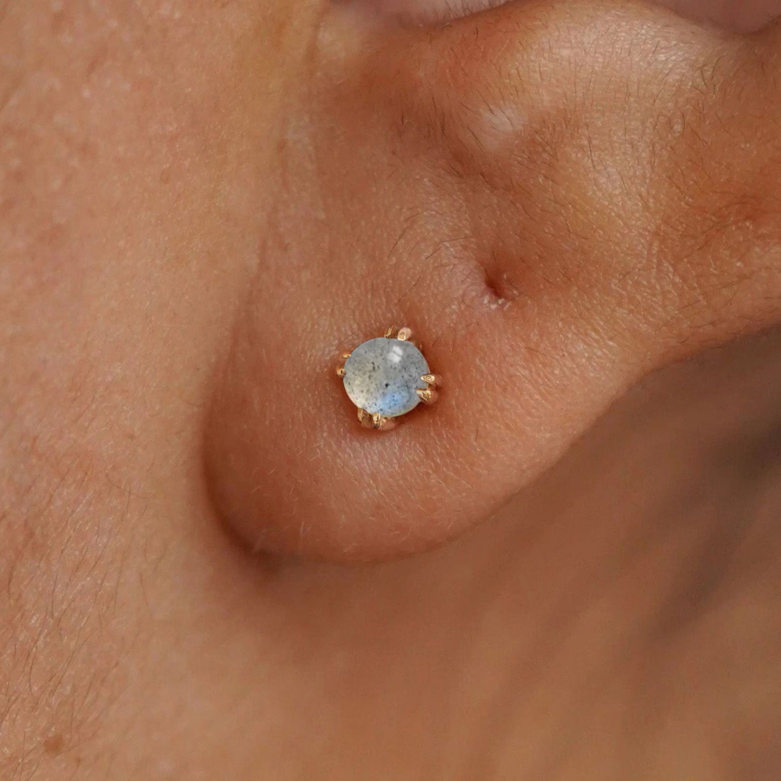 Close up view of a model's ear wearing a yellow gold labradorite earring