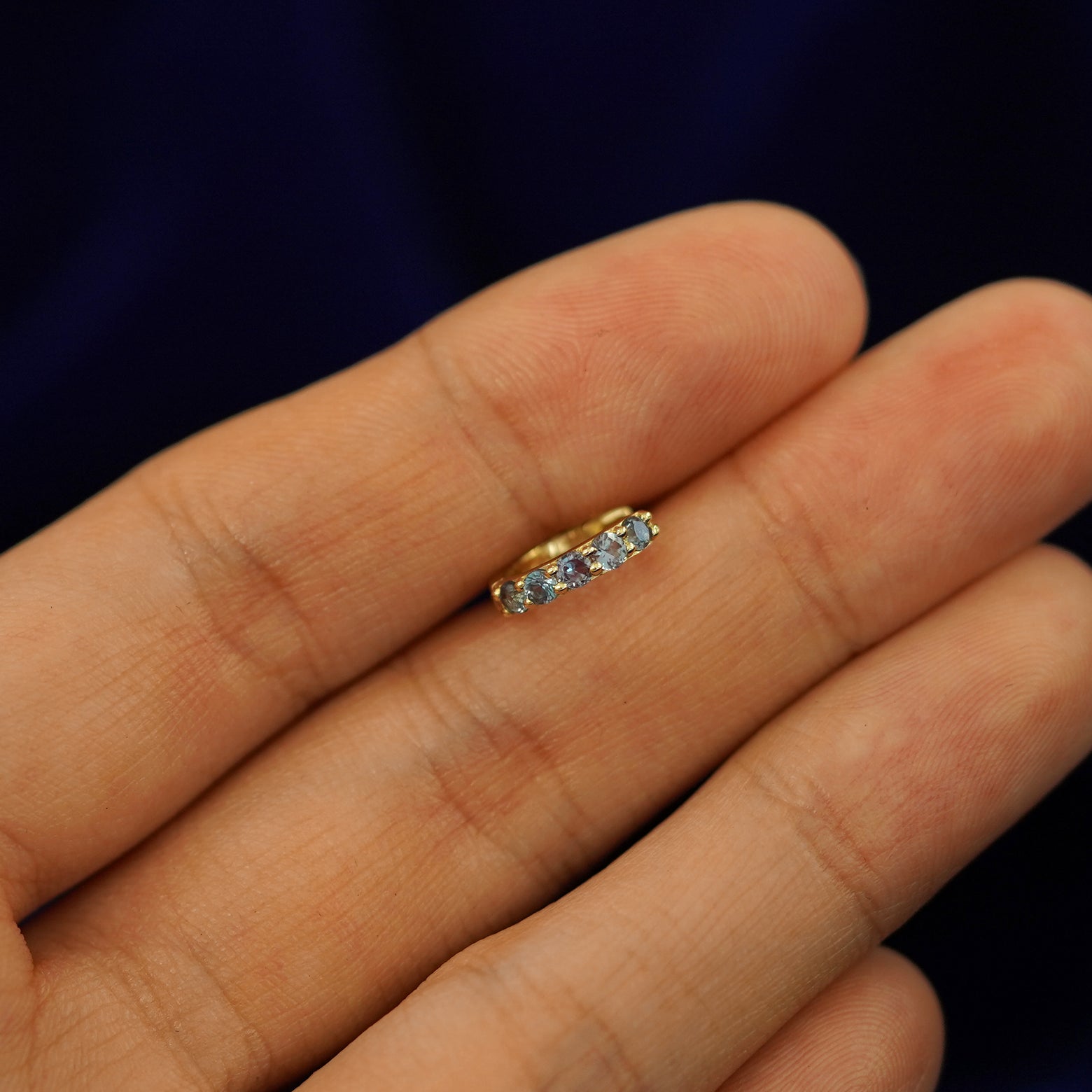 A small Alexandrite huggie hoop earring between a model's fingers to show the gems