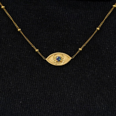 Close up view of a solid 14k yellow gold alexandrite evil eye necklace against a model's black shirt