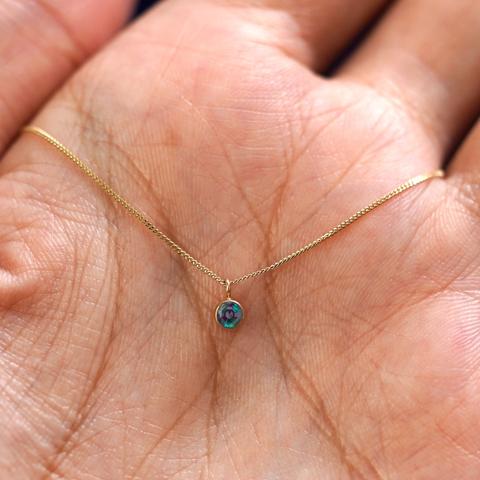 A solid 14k gold Alexandrite Necklace resting in a models palm