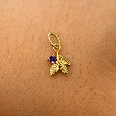A solid 14k yellow gold amethyst Gemstone 3 Leaves Charm resting on the back of a model's hand