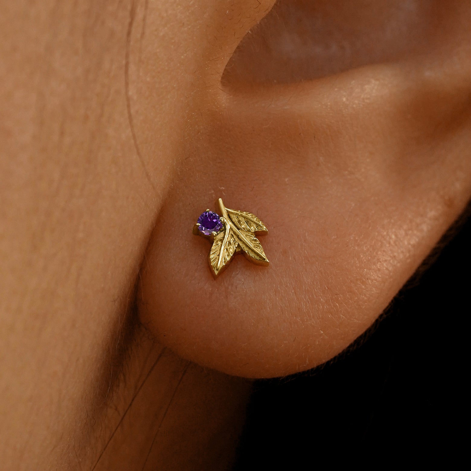 Close up view of a model's ear wearing a 14k yellow gold amethyst 3 Leaves Gemstone Earring
