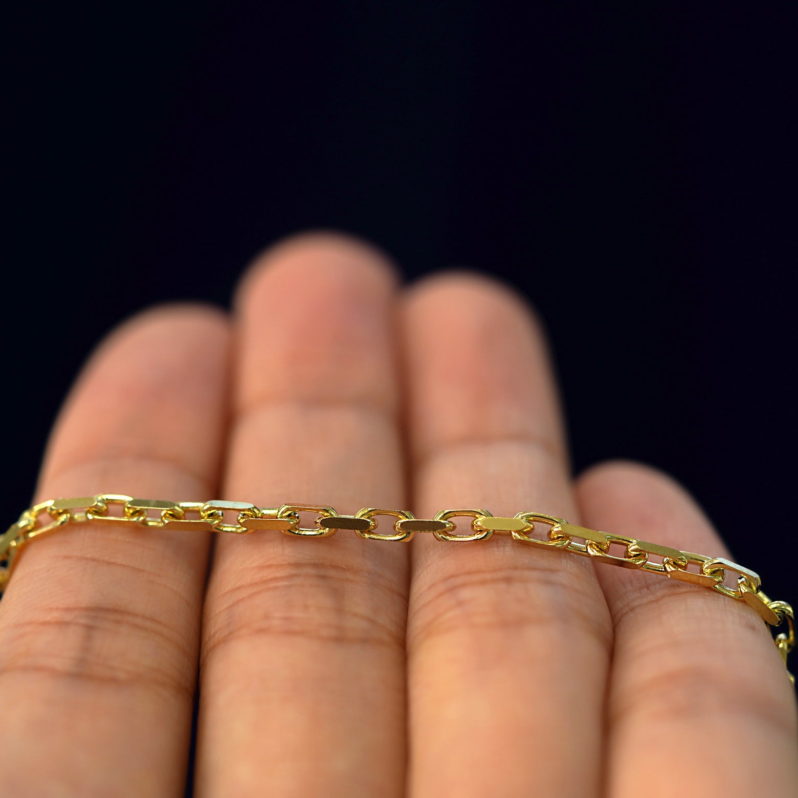 A yellow gold Anchor Anklet resting on a model's fingers