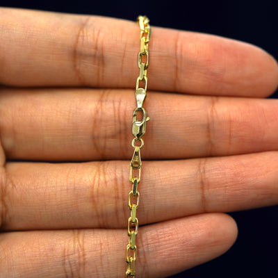A model's hand holding a yellow 14k gold Anchor Chain with a lobster claw clasp