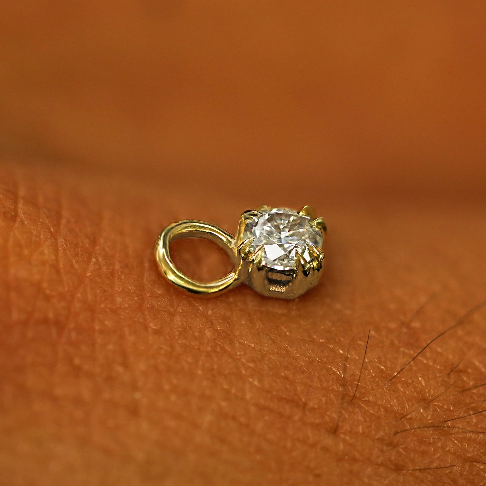 A solid yellow gold Diamond Charm for earring resting on the back of a model's hand