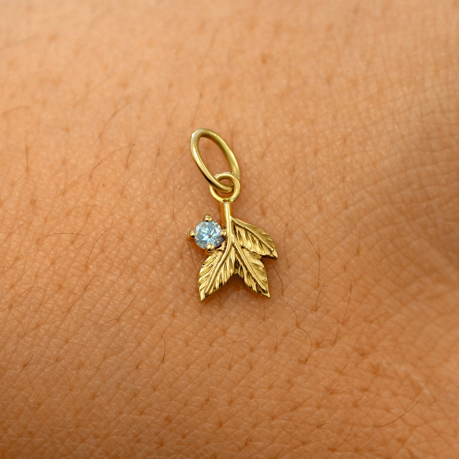 A solid 14k yellow gold aquamarine Gemstone 3 Leaves Charm resting on the back of a model's hand