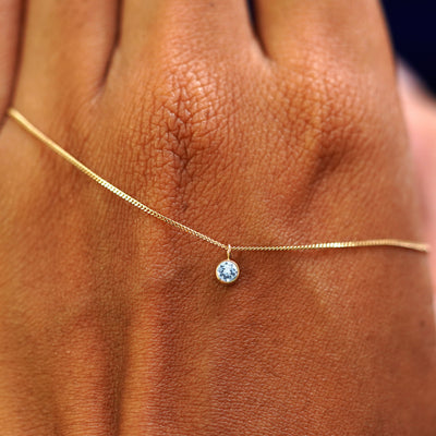 A solid yellow gold Aquamarine Necklace draped across the back of a model's hand