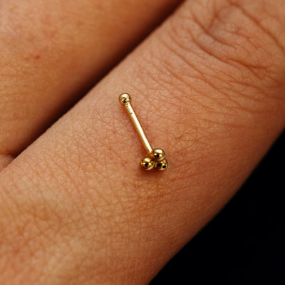 Close up view of a single 14k solid gold Ball Trio Nose Stud with a ball end backing resting on the back on a model's hand