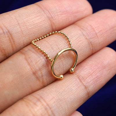A solid 14 karat yellow gold Line Cuff with Chain earring resting on a model's finger