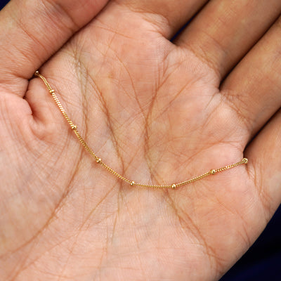 A yellow gold Beaded Essential Chain draped on a model's palm