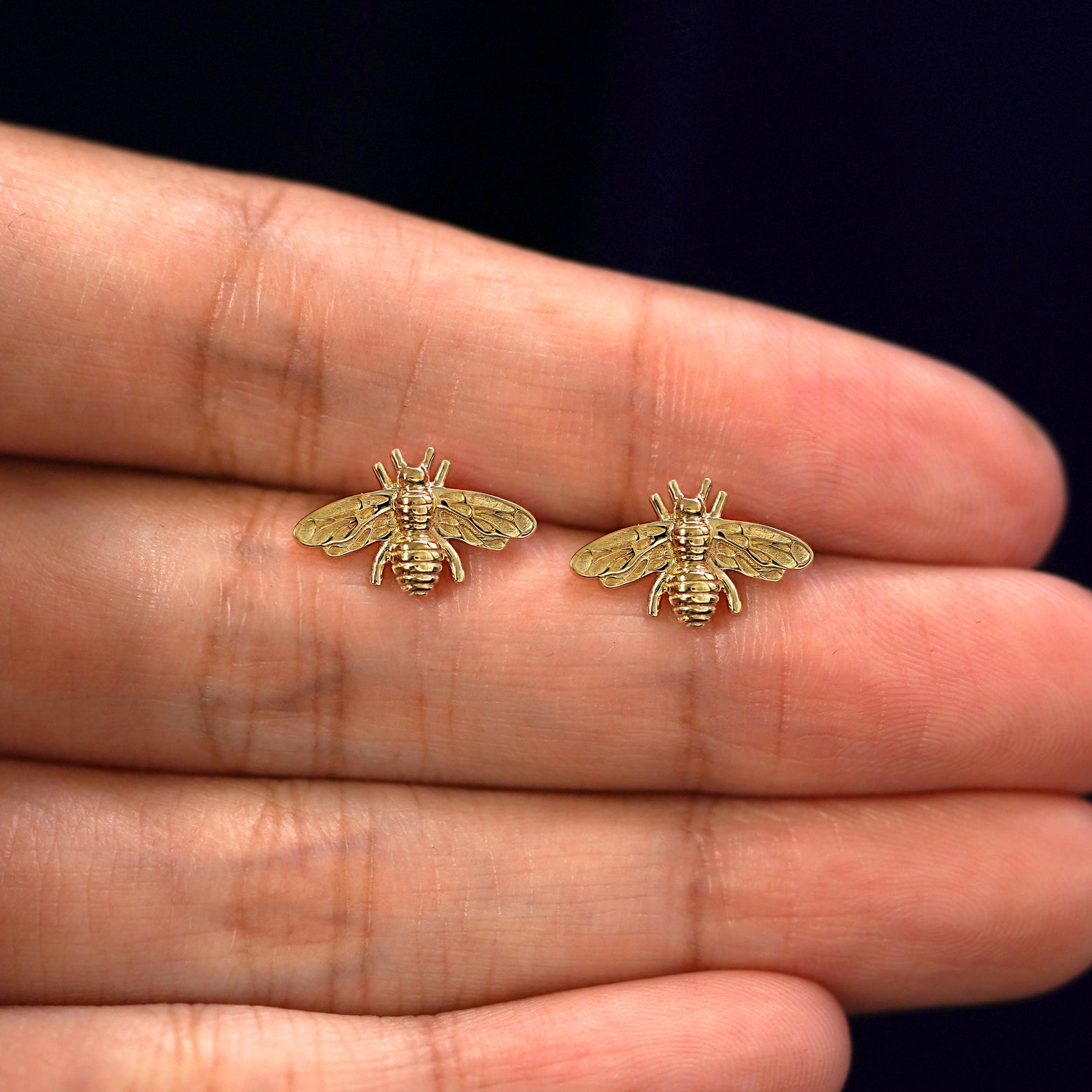 A model's hand holding a pair of recycled 14k gold Bee Earrings