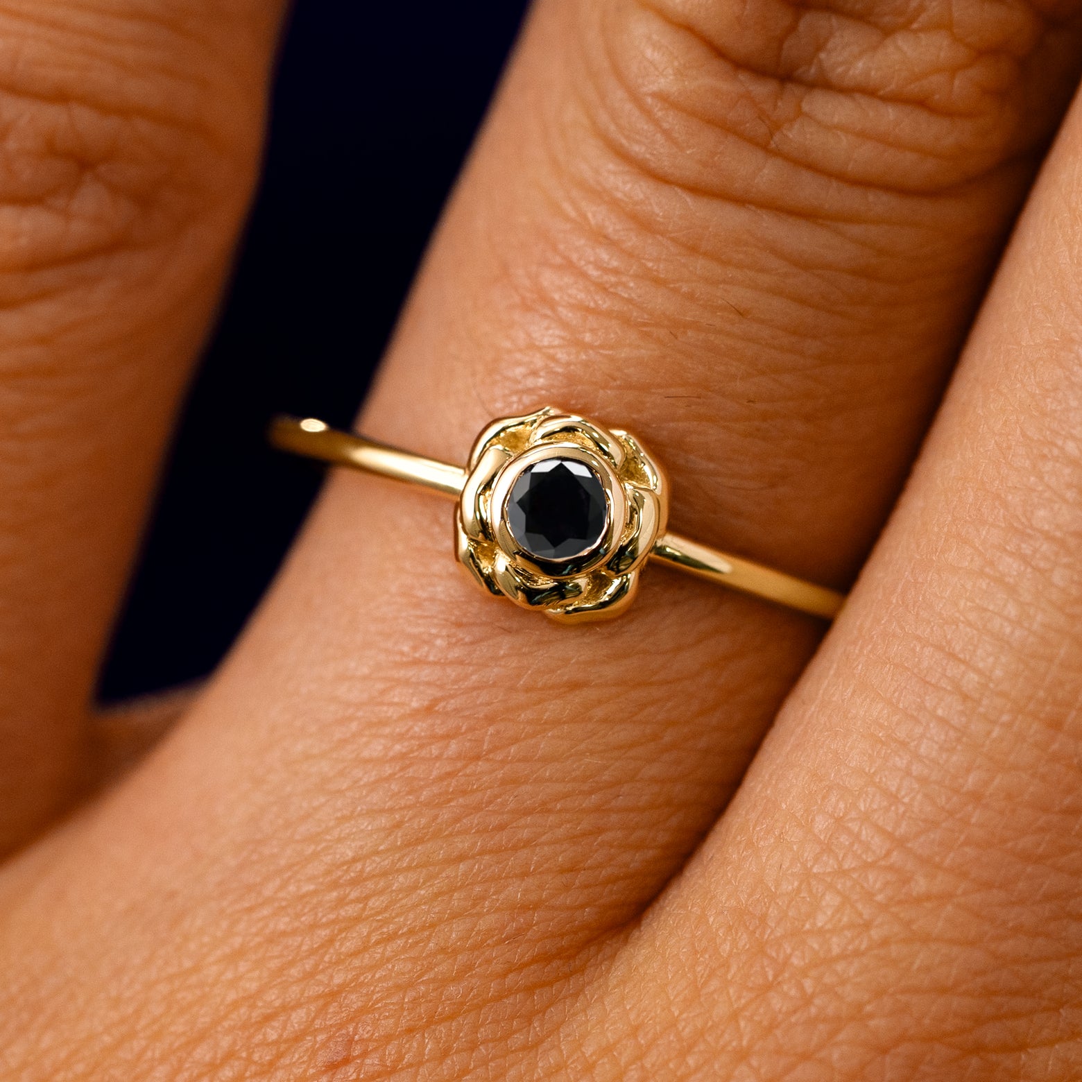 A solid 14k yellow gold Black Diamond Flower Ring on a model's finger