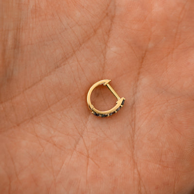 A closed black diamond huggie hoop laying in a models palm