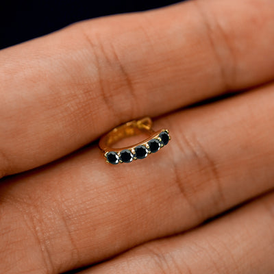 A small Black Diamond huggie hoop earring between a model's fingers to show the gems
