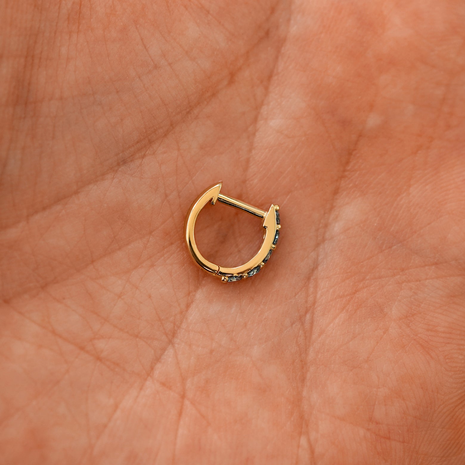 A closed lab light blue diamond huggie hoop laying in a models palm