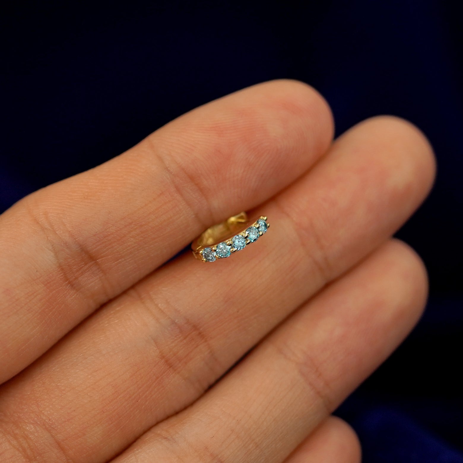 A small Light Blue Lab Diamond huggie hoop earring between a model's fingers to show the gems