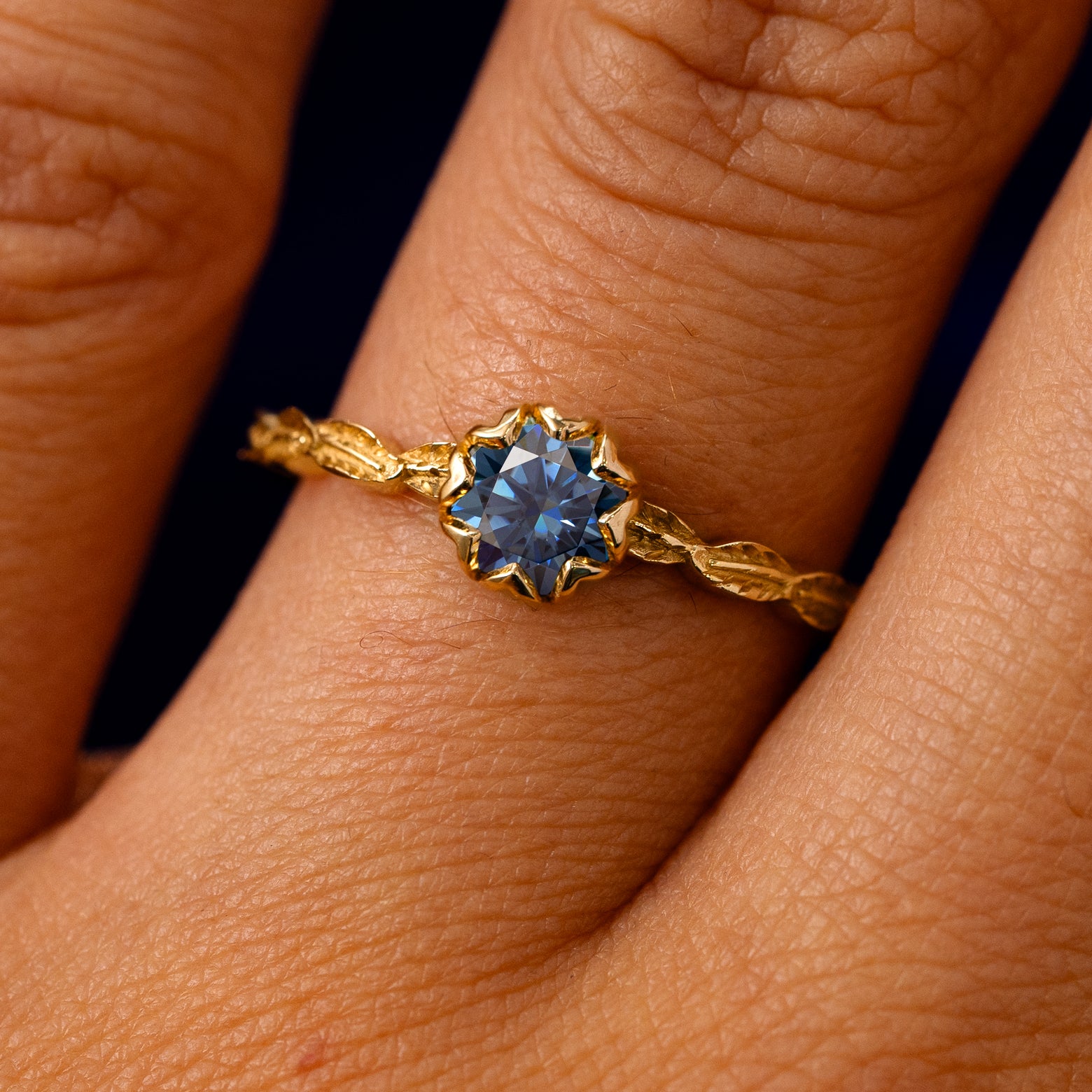 A solid 14k yellow gold Blue Moissanite Leaf Ring on a model's finger