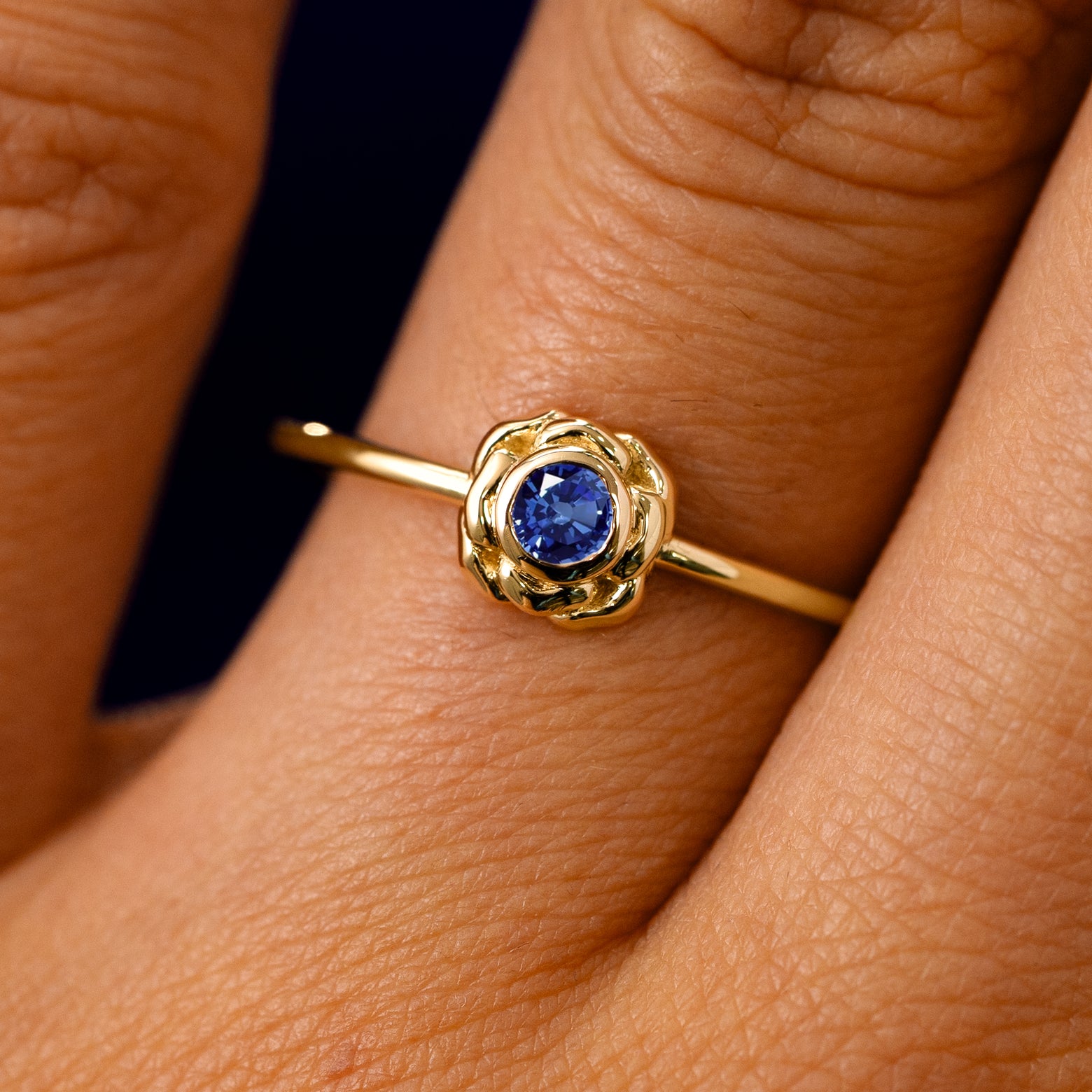 A solid 14k yellow gold Blue Sapphire Gemstone Flower Ring on a model's finger