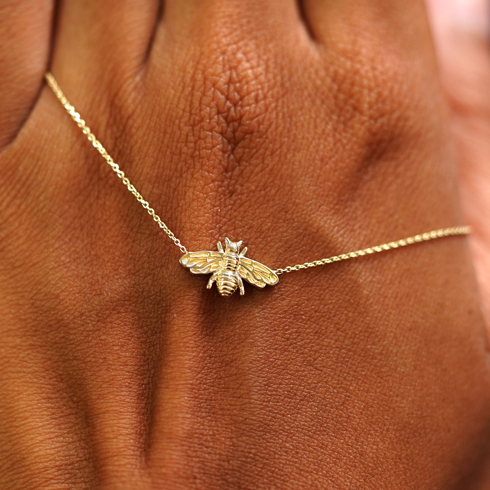 A solid gold Bee Necklace resting on the back of a model's hand