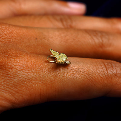 A 14k yellow gold Butterfly Charm for chain balancing on the back of a model's finger