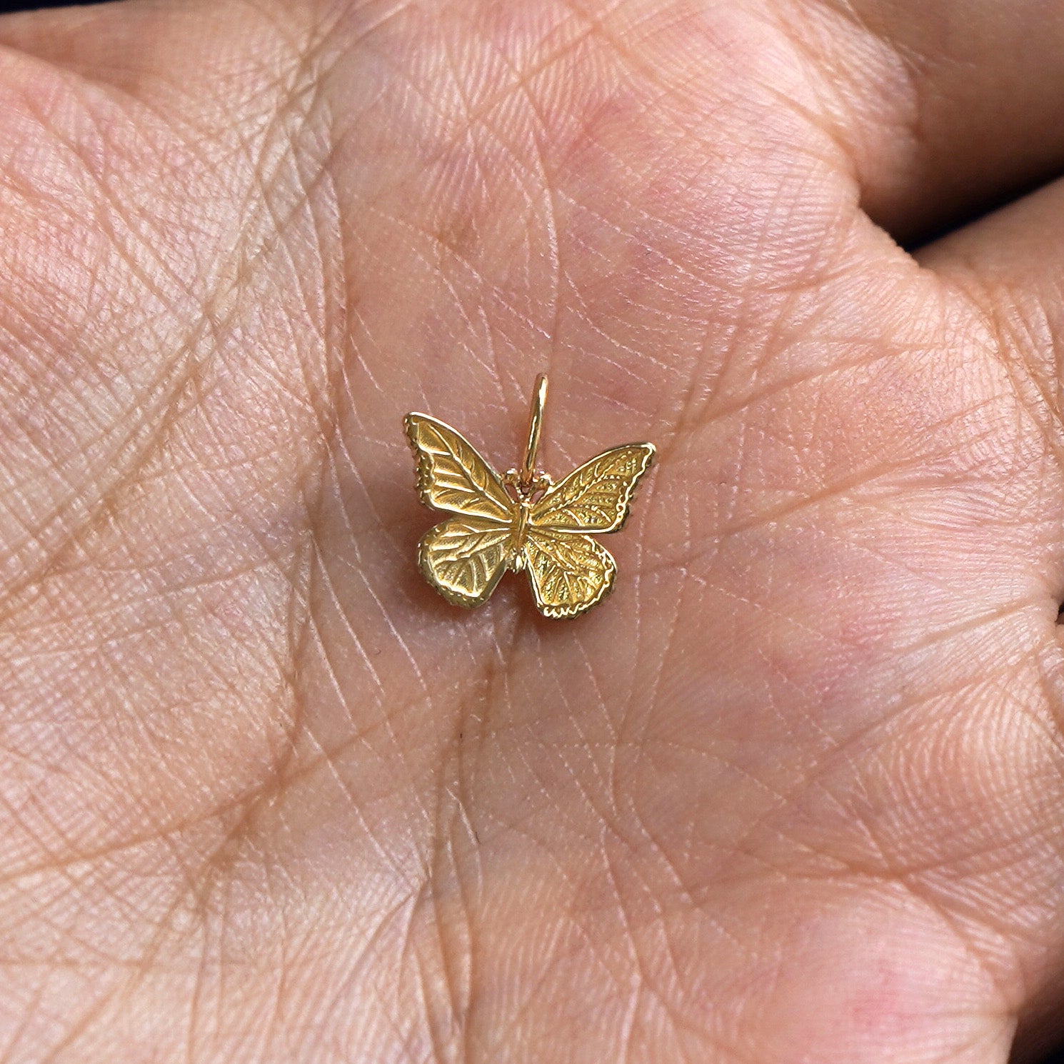 A solid gold Butterfly Charm for chain resting in a model's palm