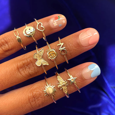 Close up view of three fingers with a colorful manicure wearing various Automic Gold rings including a Butterfly Ring