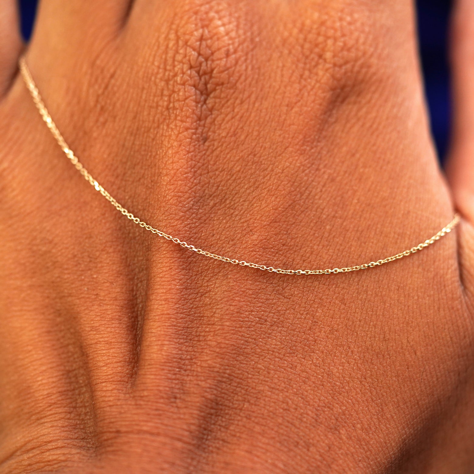 A solid yellow gold Cable Anklet resting on the back of a model's hand