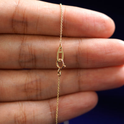 A model's hand holding an Automic Gold AU spring ring lock on a yellow gold Cable Bracelet