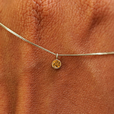 Close up view of a 14k champagne gold Citrine Necklace draped across the back of a model's hand