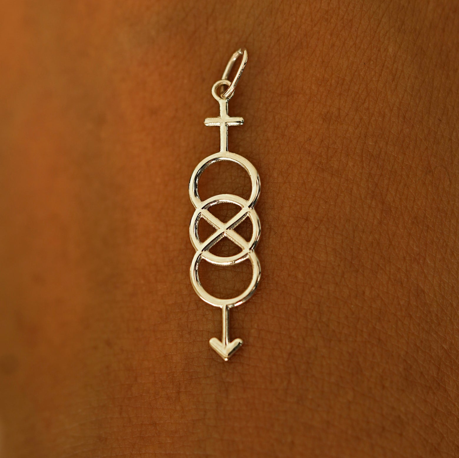 A solid 14k champagne gold Bisexual Symbol Charm resting on the back of a model's hand