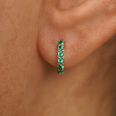 Close up view of a model's ear wearing a champagne gold Small Emerald Huggie Hoop