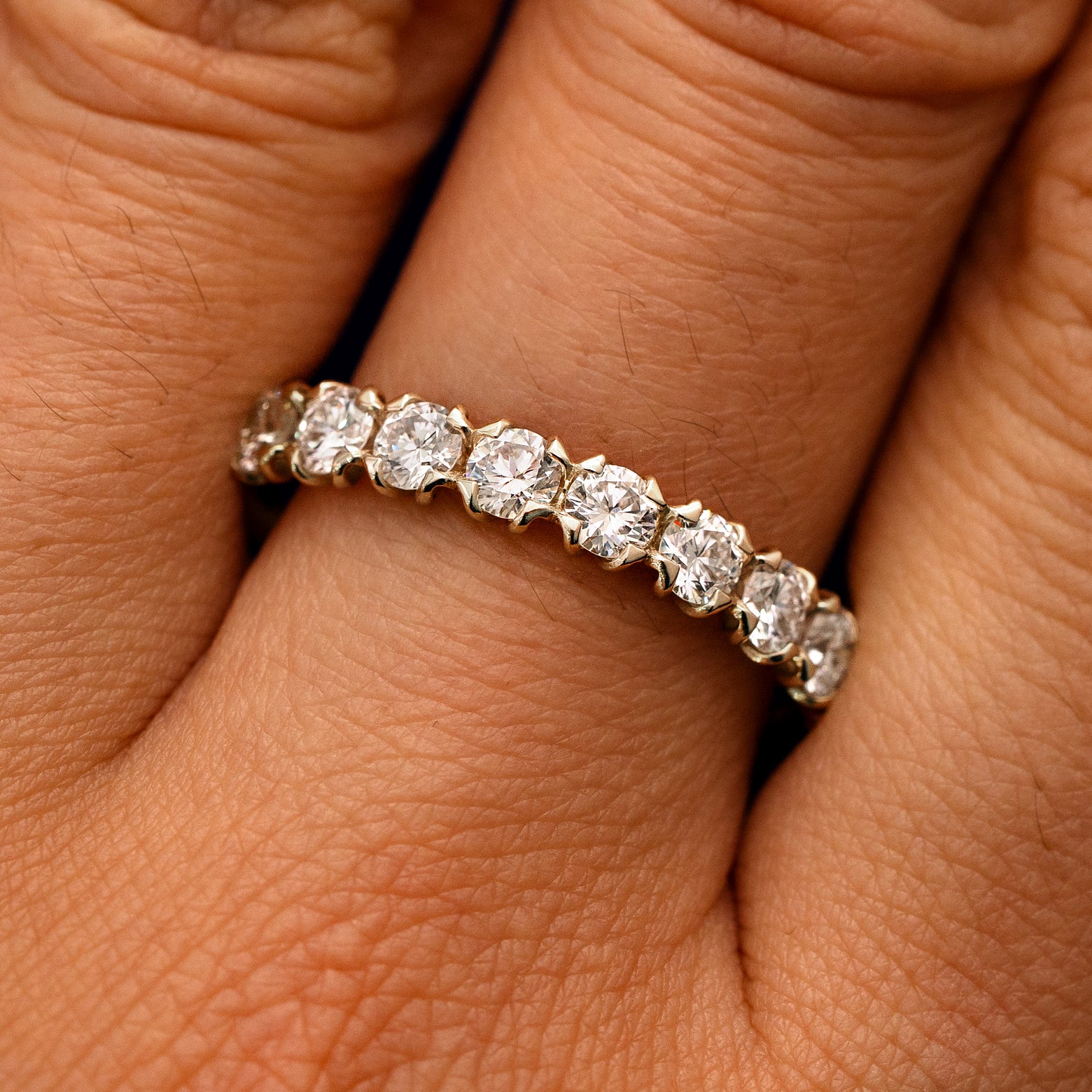 Close up view of a model's fingers wearing a 14k champagne gold Petal Set Diamond Eternity Band