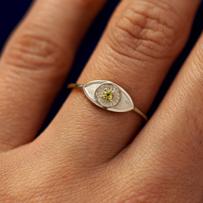 Close up view of a model's hand wearing a champagne gold Evil Eye Ring in the Emerald gemstone option